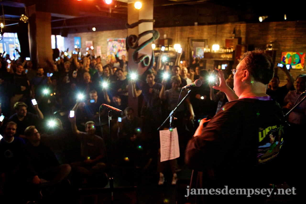 James Dempsey takes a photo of the full-house crowd raising their iPhones high
